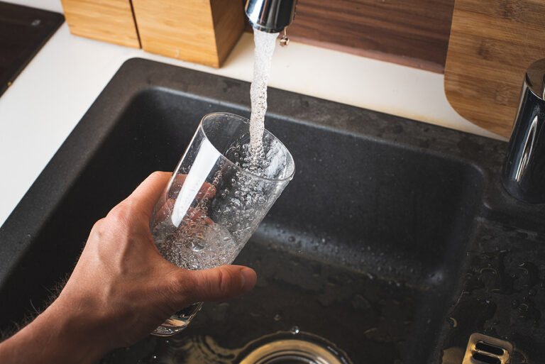 A person filling a glass from a kitchen faucet.