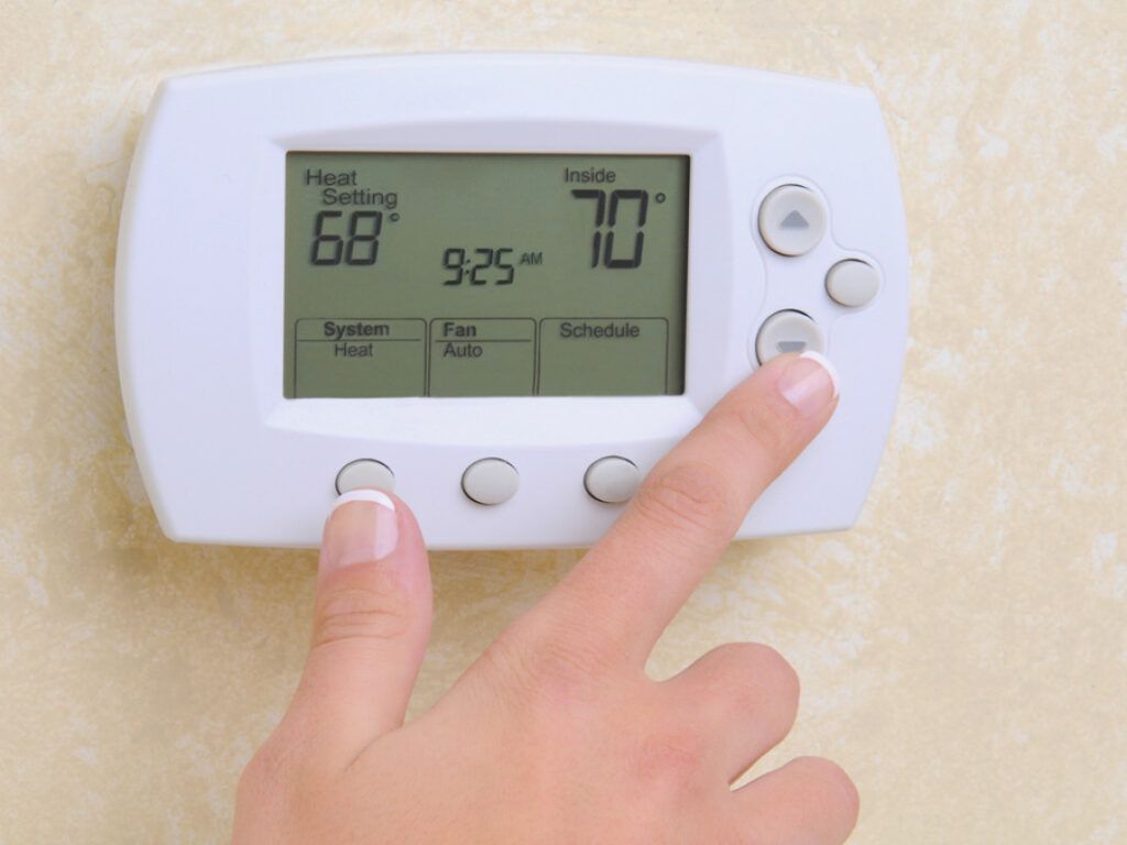 A person's hand using a digital thermostat.