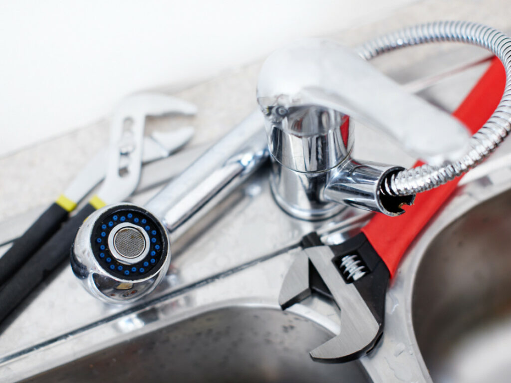 A newly installed kitchen faucet with wrenches laid next to it.