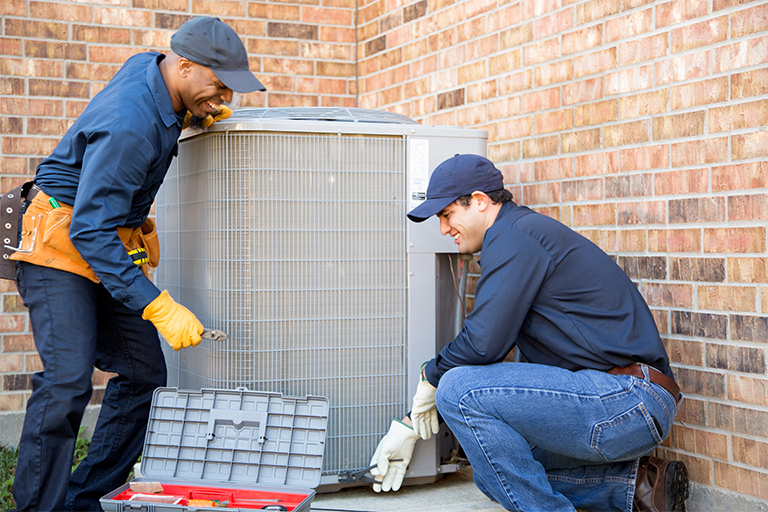 two hvac technicians repairing an outdoor HVAC unit